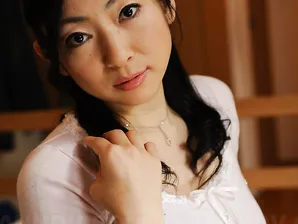 Slender mature Japanese woman Emiko Koike bends over to pose in white dress